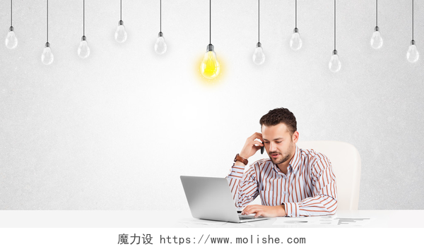坐在办公桌前用笔记本电脑工作的商人商人坐在桌旁，手里拿着灯泡
